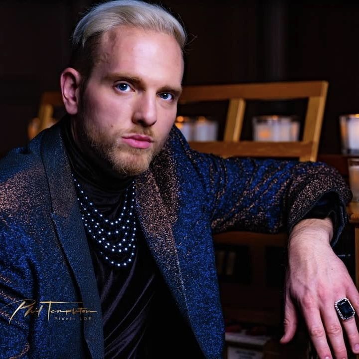 Stephen Aber in a blue sparkle jacket with layered pearl necklaces and a large black statement ring