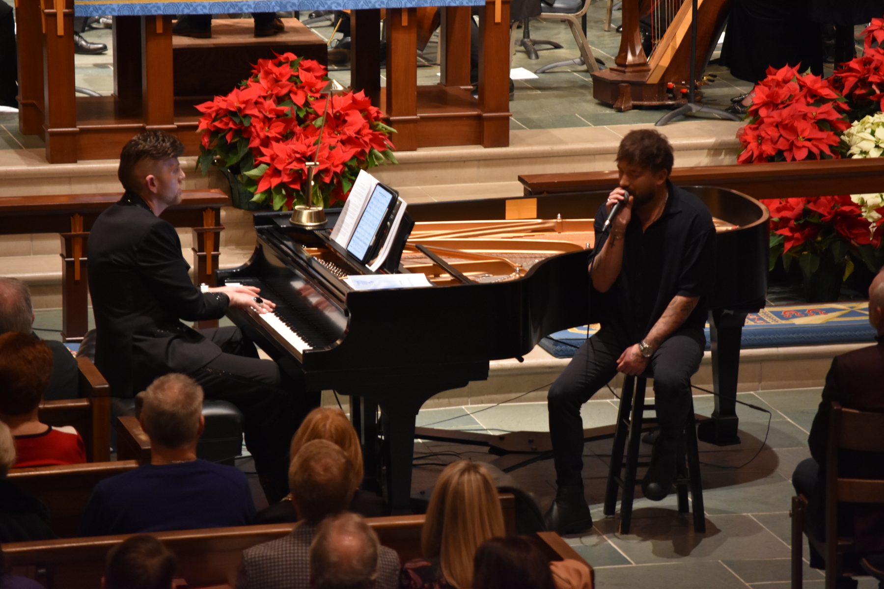 Stephen Aber at a grand piano accompanying a singer during a Christmas concert, with poinsettias on the chancel and an audience in the pews