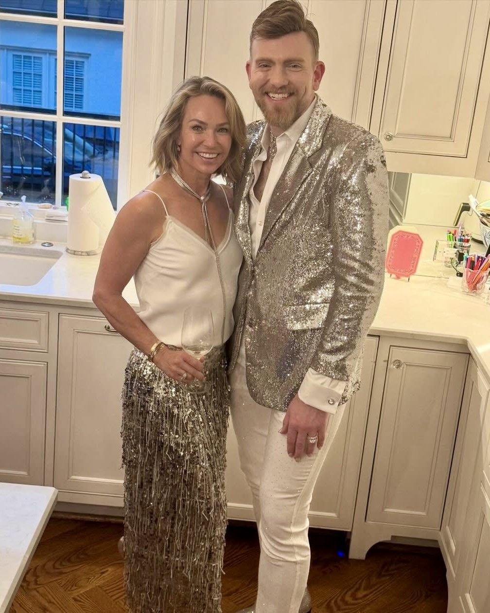 Stephen Aber in a silver sequin jacket, posing with a friend in a kitchen