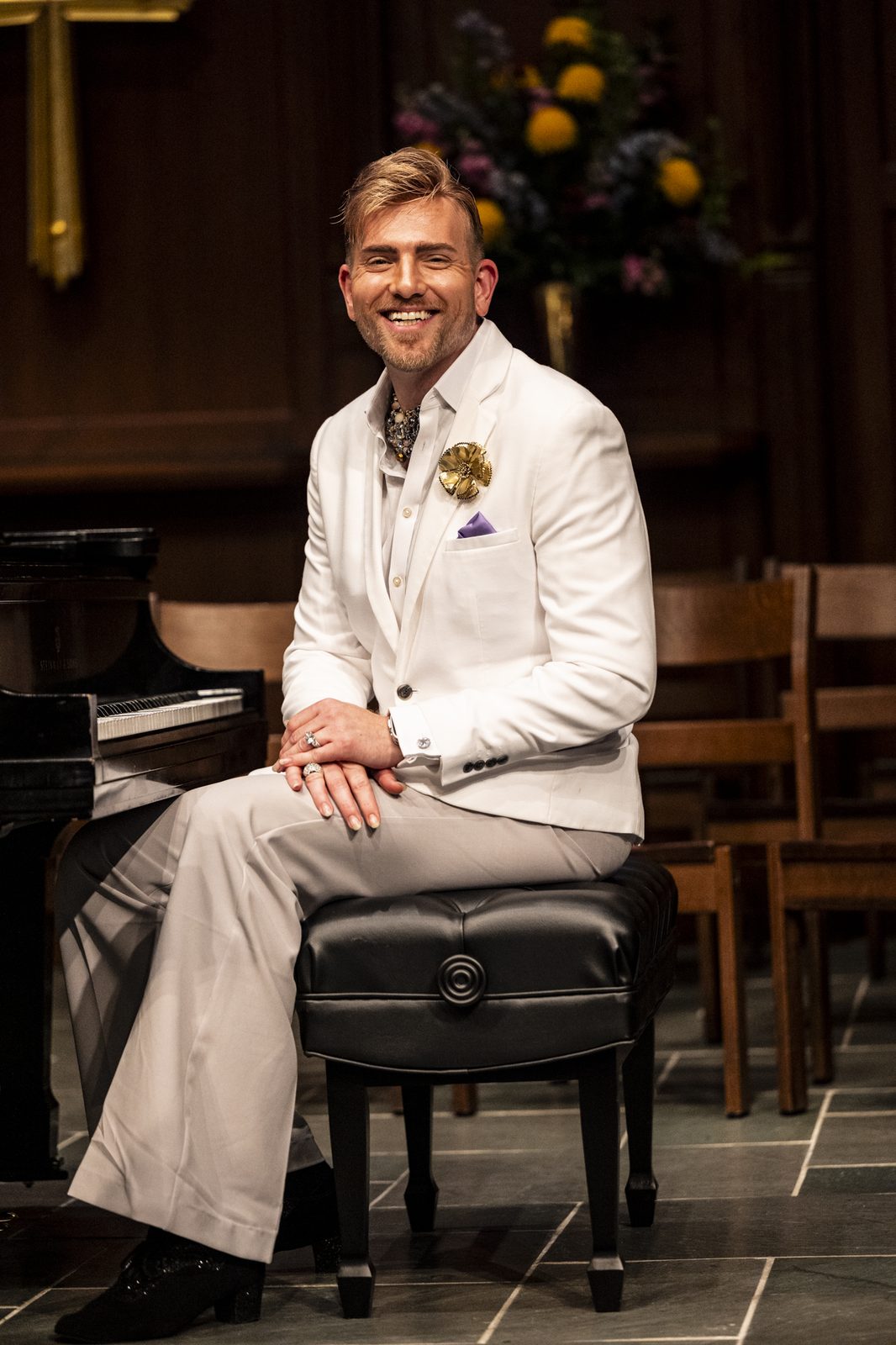 Stephen Aber in a white suit seated on a piano bench